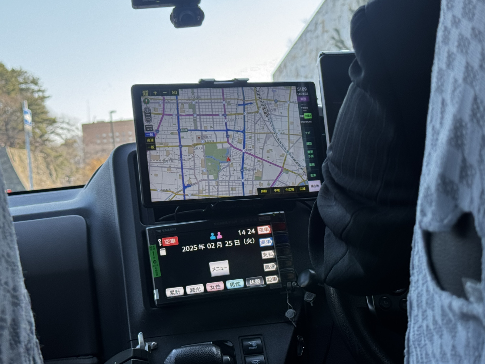 タクシー車内でタブレットを操作し、営業データを確認する日本人ドライバー。努力が見える給与制度を表現した写真。